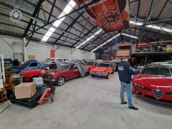 An AFP investigator stands in a shed in front of several cars partially covered with cloths