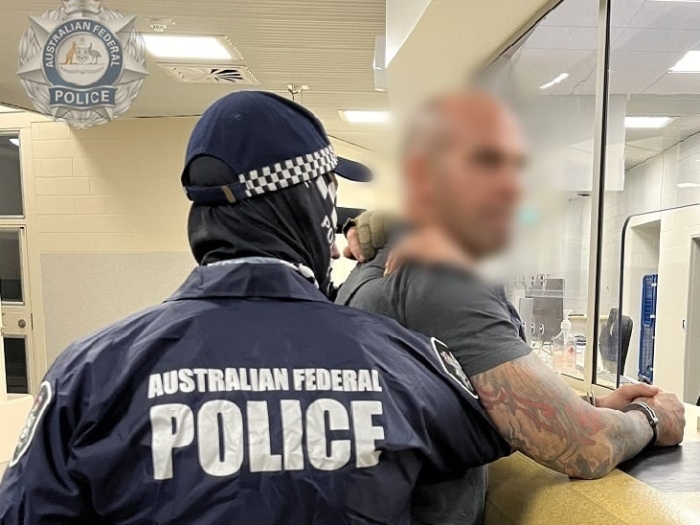 A man in a grey shirt is restrained by AFP officers.