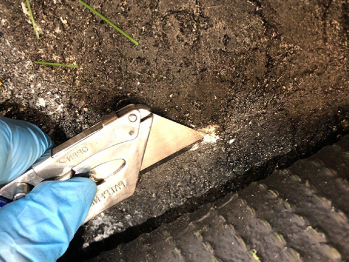 Hand using retractable blade to cut into synthetic turf 